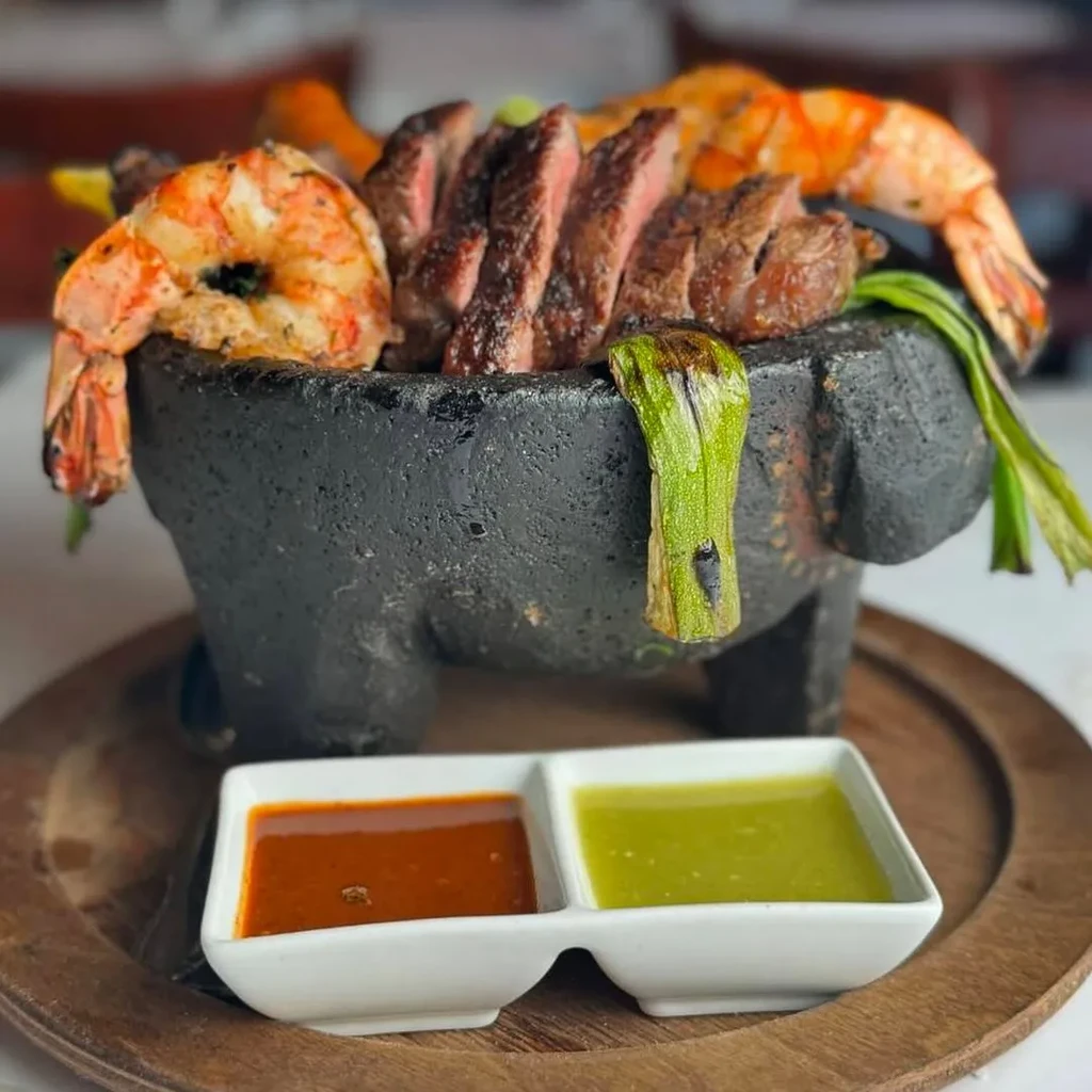 Grilled shrimp and sliced steak in a molcajete with sauces.