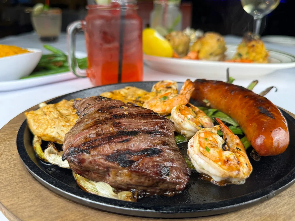 A sizzling platter with steak, shrimp, sausage, and chicken on onions.
