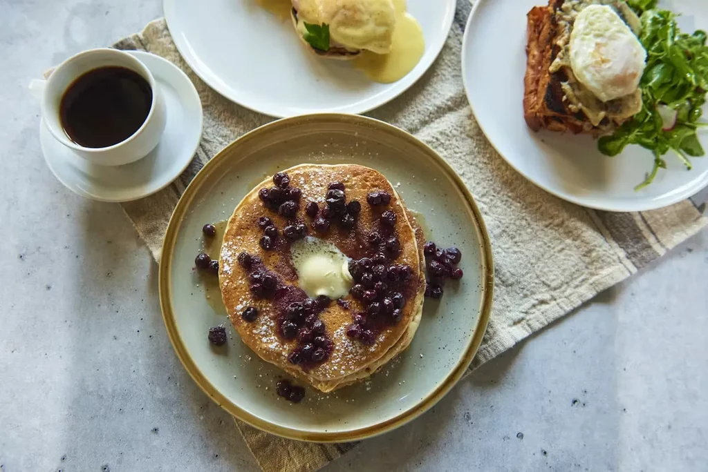 Pancakes with blueberries and butter, eggs Benedict, and avocado toast with coffee.