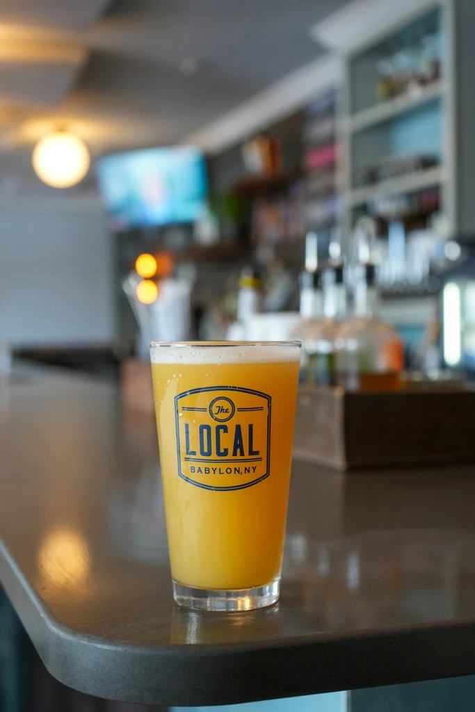Cold hazy beer with 'The LOCAL' logo on a bar.