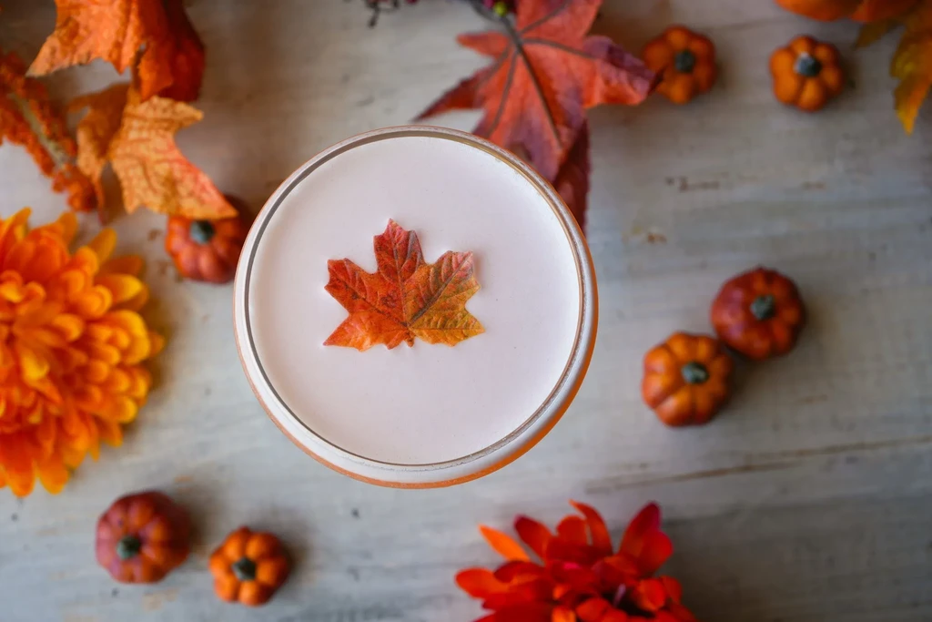 Top-down foamy cocktail with artificial maple leaf garnish and autumn decor.