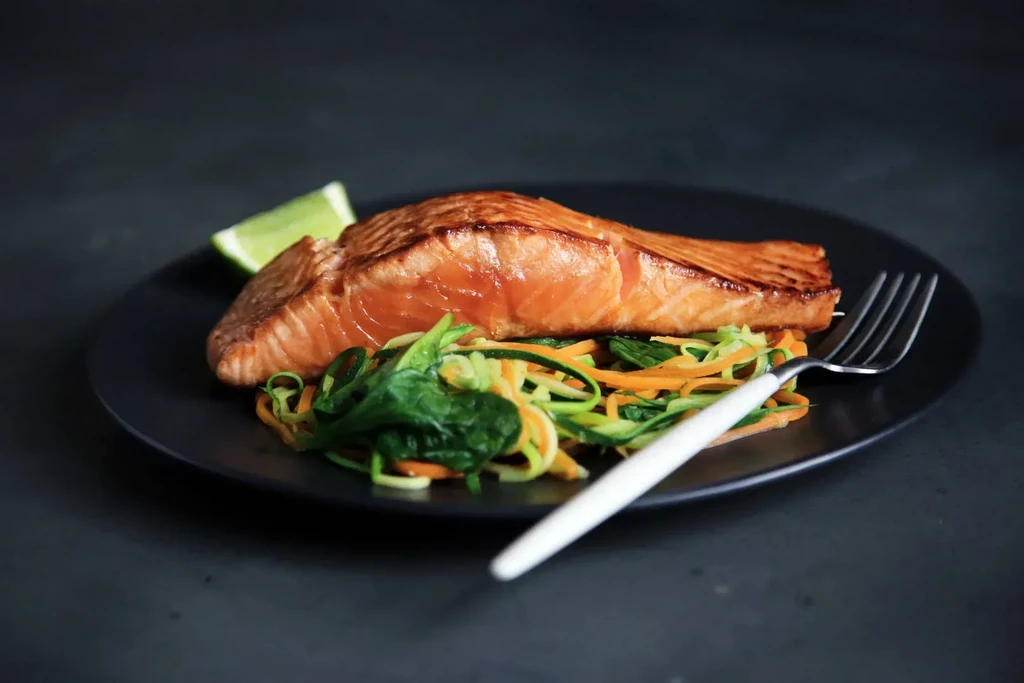 Salmon fillet with zucchini noodles and lime on a black plate.