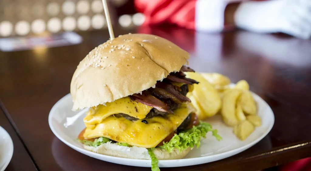 A double cheeseburger with bacon and fries on a white plate.