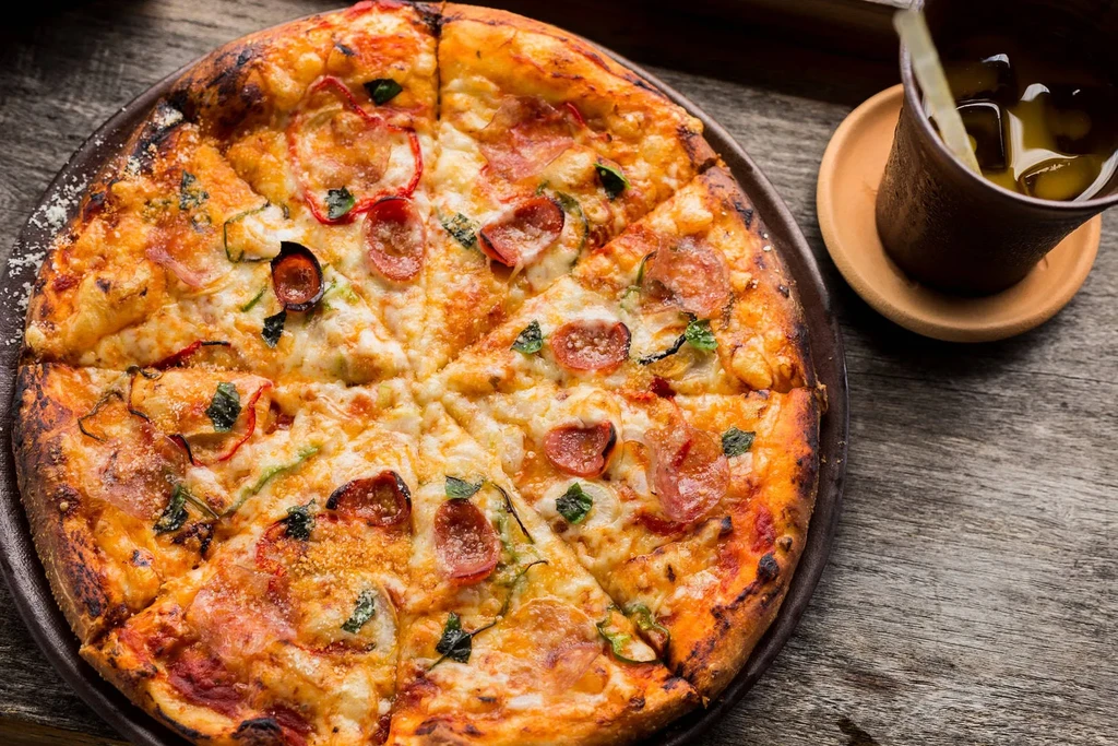 A sliced pizza with pepperoni, cheese, and basil, next to a drink.