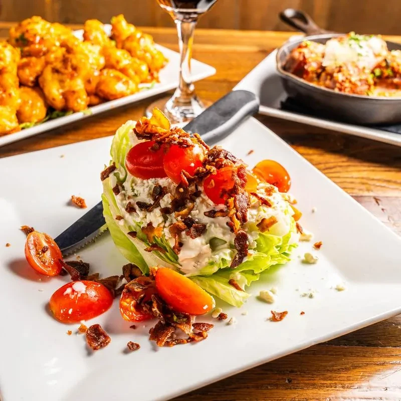 A wedge salad with tomatoes, bacon bits, and blue cheese crumbles.