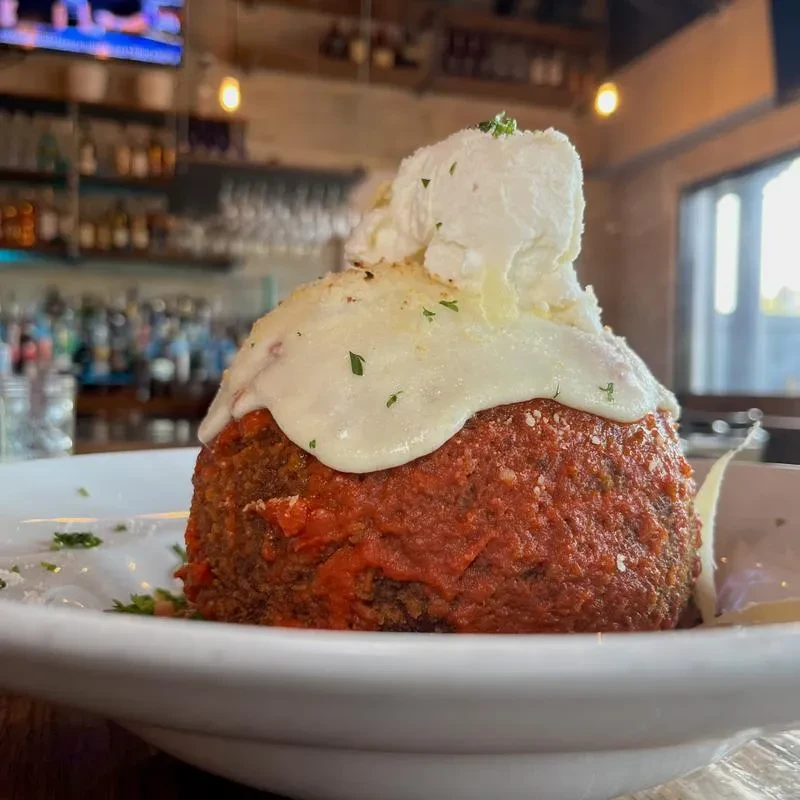 A large meatball with tomato sauce, mozzarella, and ricotta cheese.