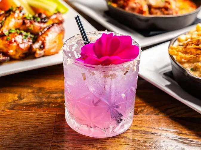 A pink cocktail with a flower and salted rim on a wooden table.