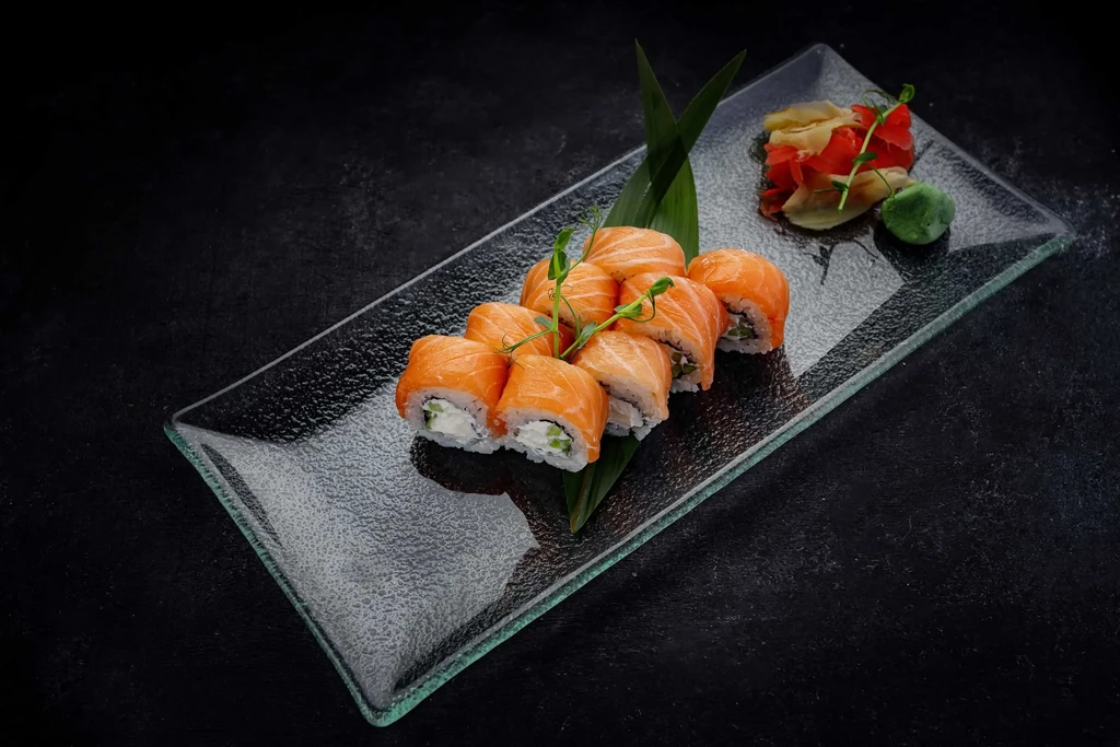 Salmon sushi rolls with pickled ginger and wasabi on a glass plate.