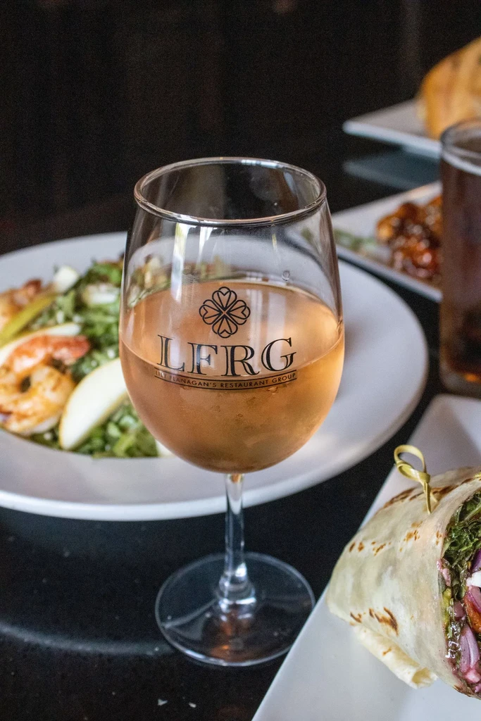Glass of rosé wine with LFRG logo and restaurant food.