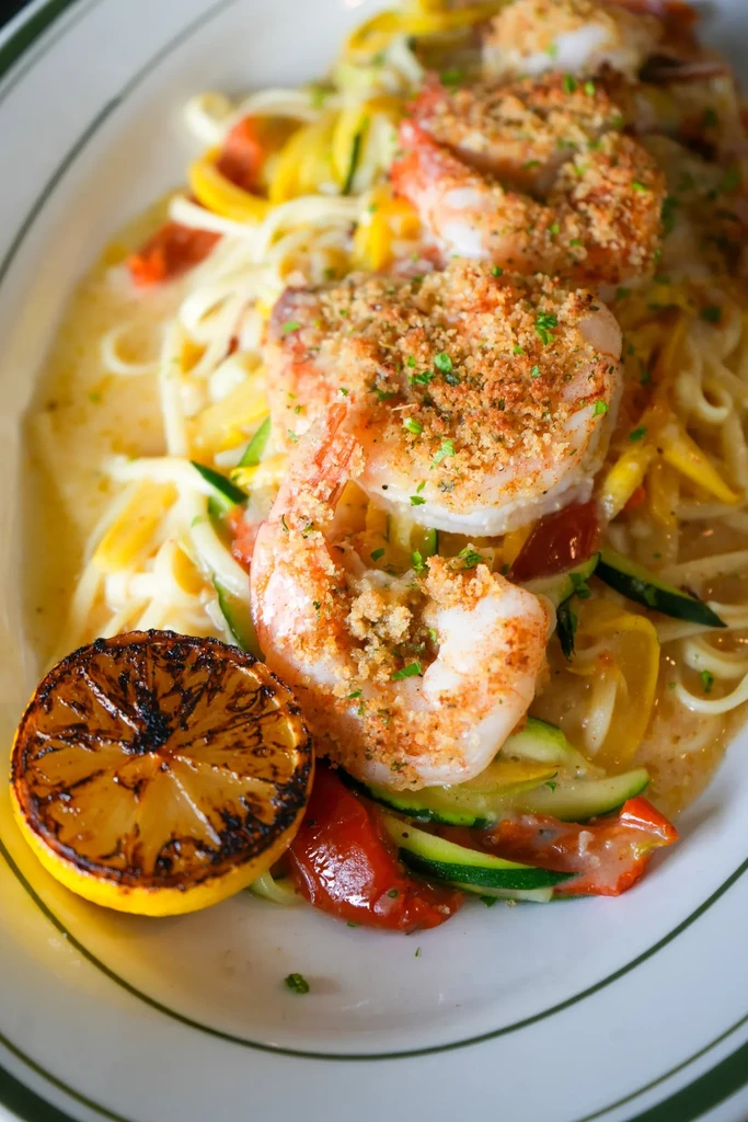 Shrimp scampi with pasta, vegetables, and a grilled lemon slice on a plate.