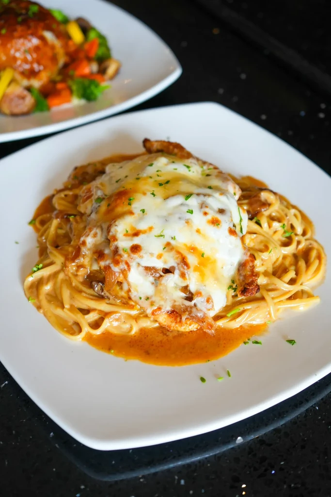 Melted cheese chicken over pasta with red sauce on a white plate.
