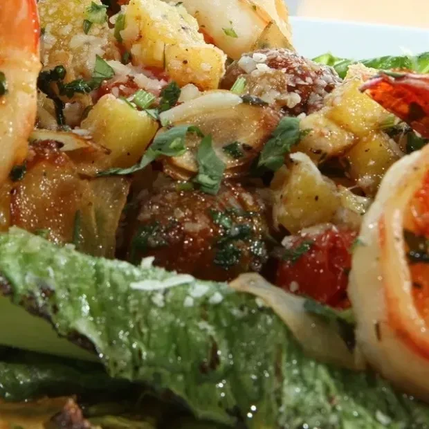 Close-up of a salad with shrimp, potatoes, tomatoes, and herbs.