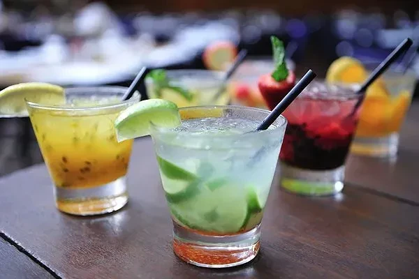 A variety of colorful alcoholic drinks with straws and fruit garnishes.
