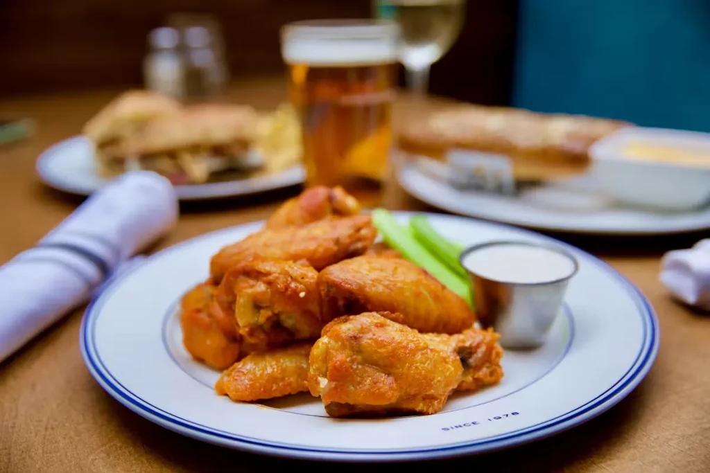 Plate of buffalo wings, celery, ranch, and drinks on a table.