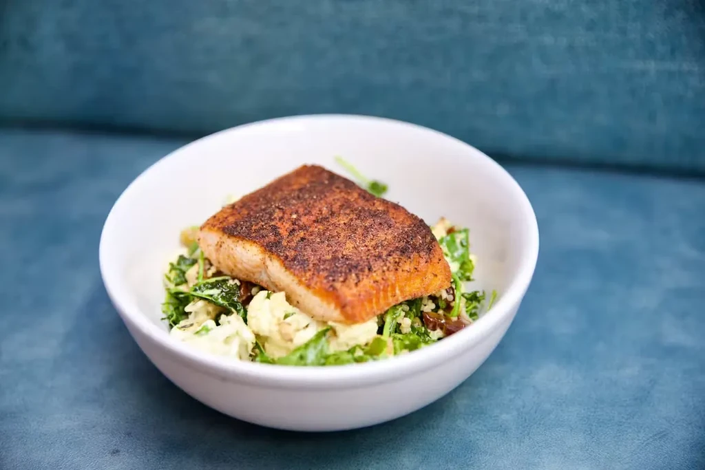 Seared salmon with kale salad in a white bowl.