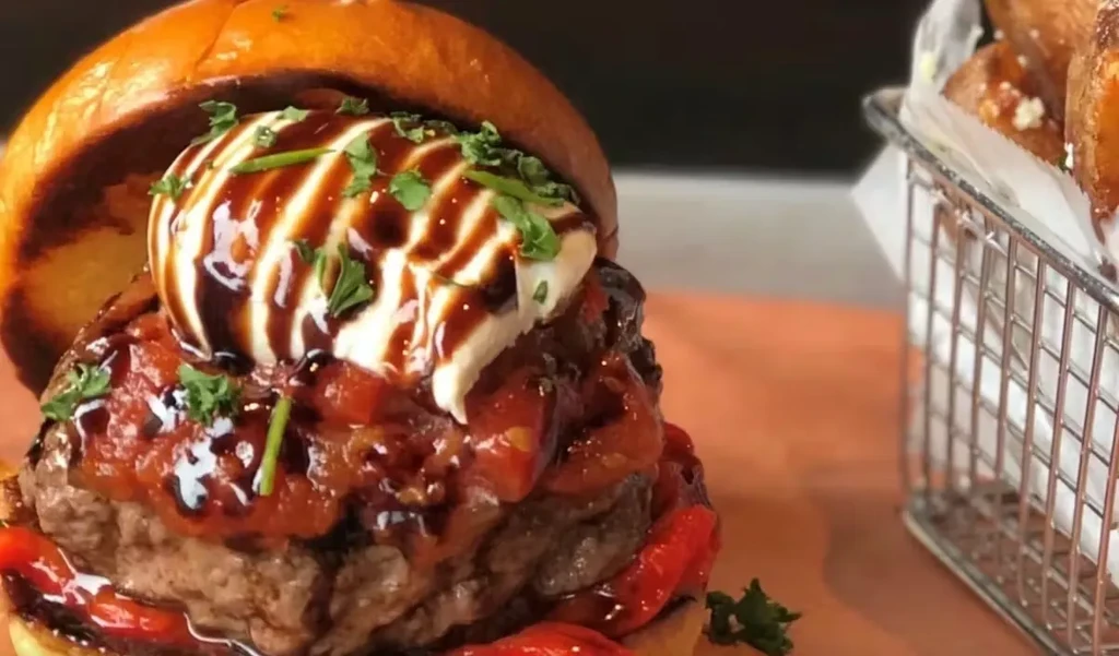 Close-up of a burger topped with sauce, cheese, and roasted peppers.