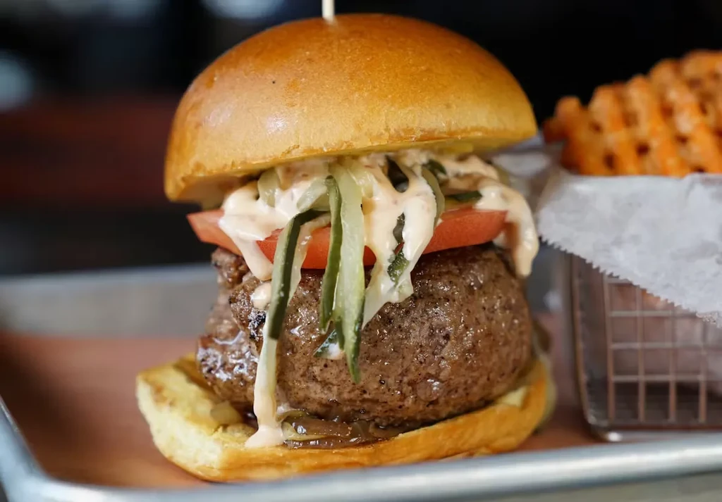 A juicy burger with tomato, pickles, and sauce, with waffle fries.