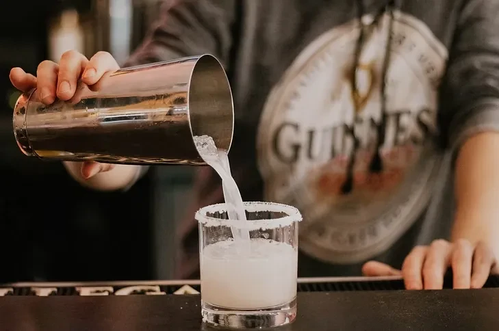 A bartender pours a drink from a shaker into a salted glass.