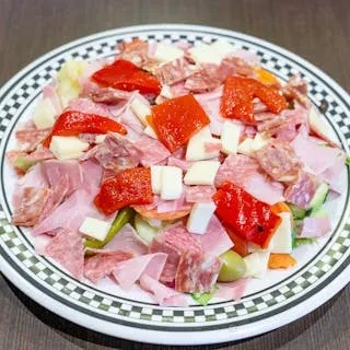 A white plate holds salad with deli meats, cheeses, and roasted red peppers.