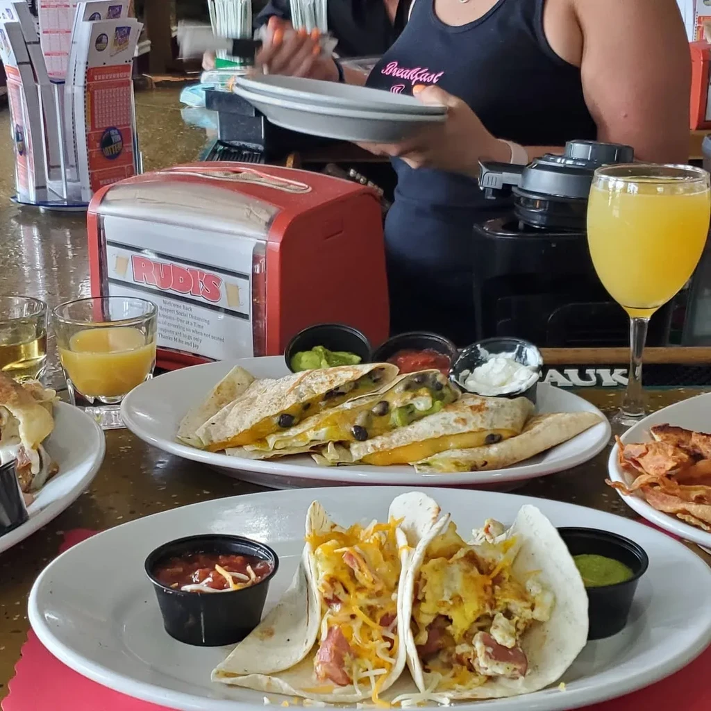Plates of breakfast quesadillas and tacos with dips, drinks, and a server.