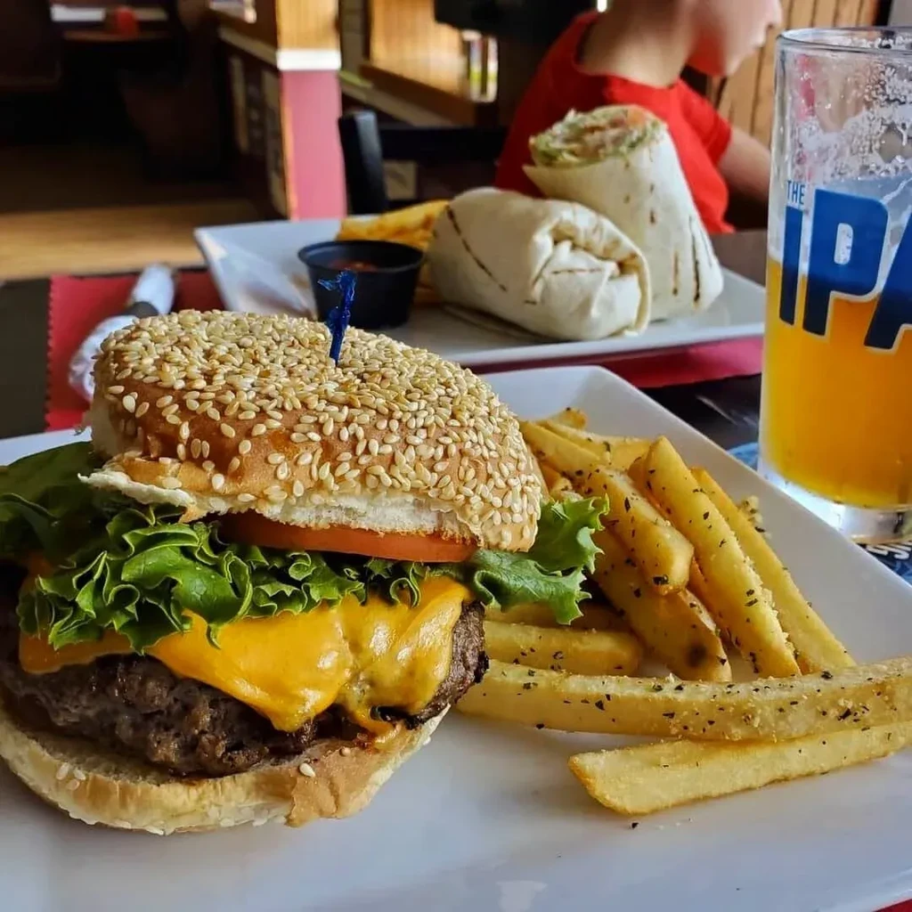 A cheeseburger and fries with a drink and wraps in the background.