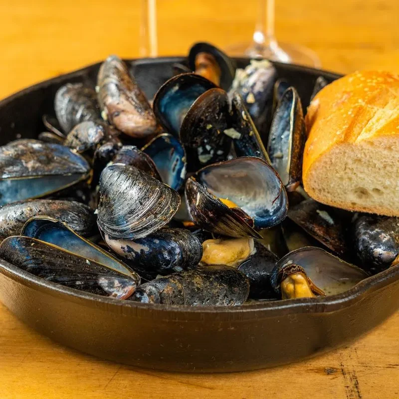 A cast-iron skillet filled with cooked mussels and a piece of bread.
