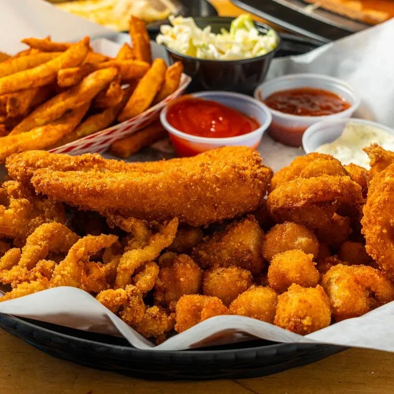 A basket of fried seafood, french fries, coleslaw, and dipping sauces.