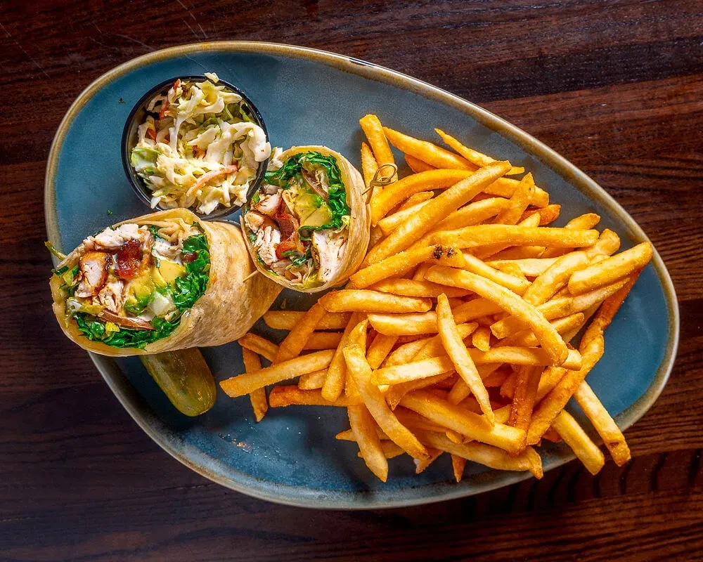 A plate with a cut wrap, fries, and coleslaw.