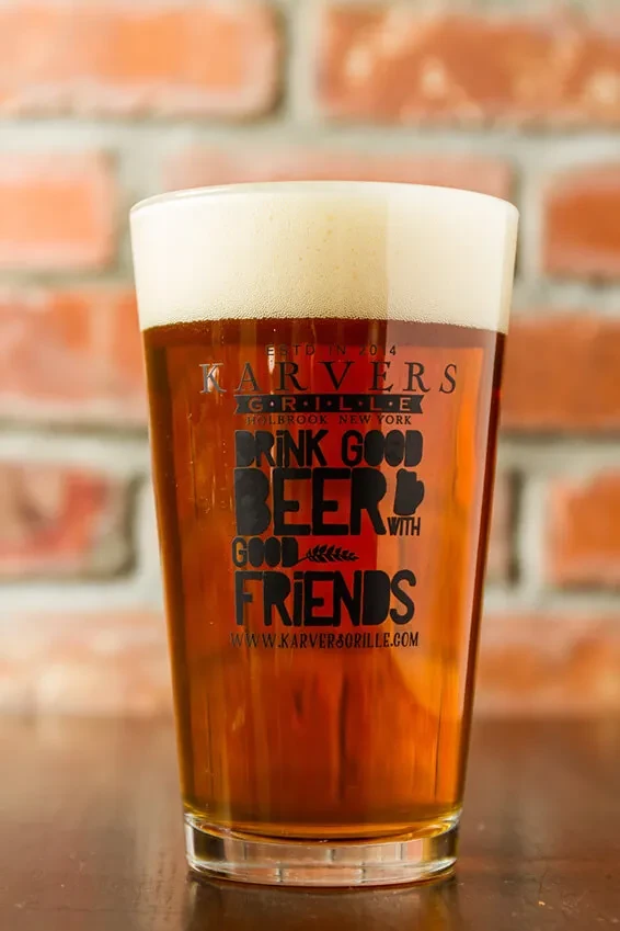 A pint glass of beer with foam, text, and a brick background.