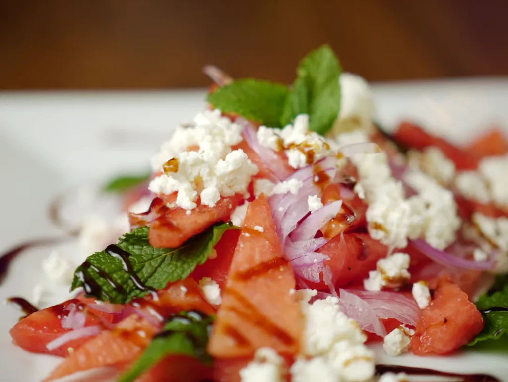 Close-up of watermelon, feta, mint, and onion salad with balsamic glaze.