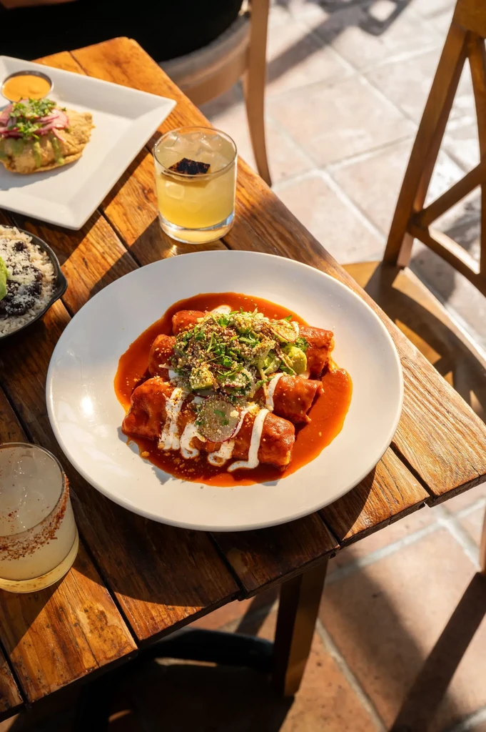 Mexican food and cocktails on an outdoor wooden table.