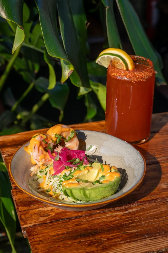 Shrimp, avocado, and pickled onions with a drink on a wooden table.