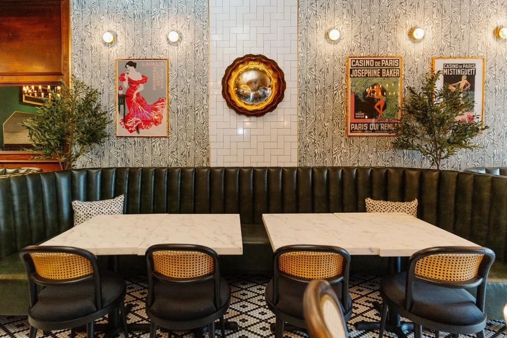 A restaurant with green leather booths, marble tables, and patterned wallpaper.
