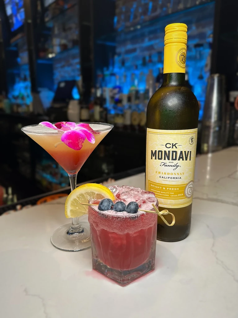 Two cocktails, a wine bottle, and bar setting on a white counter.