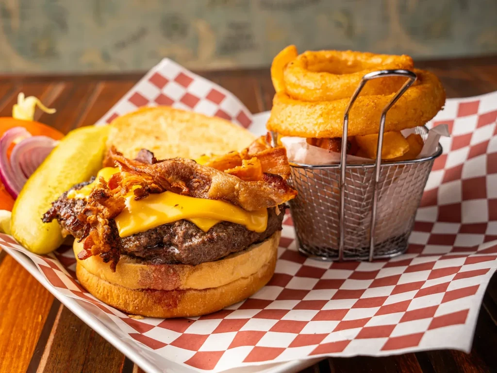 A bacon cheeseburger with a side of onion rings and a pickle.