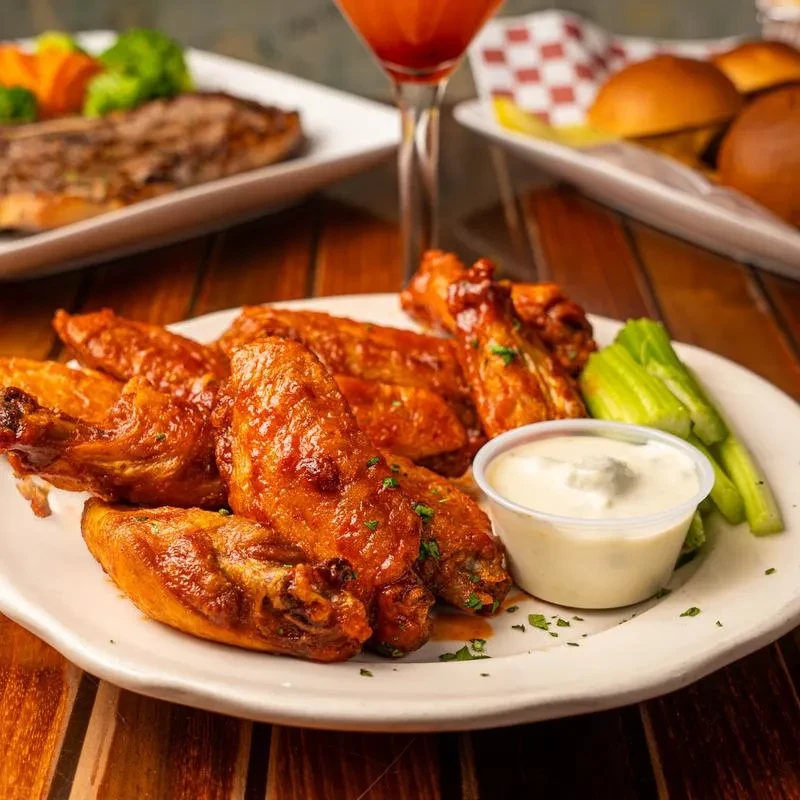 A plate of chicken wings, celery sticks, and a cup of dipping sauce.