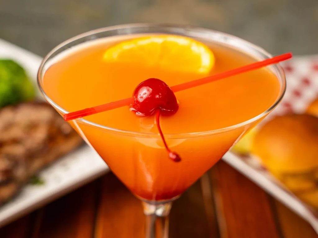 An orange cocktail with an orange slice and a cherry on a red skewer.