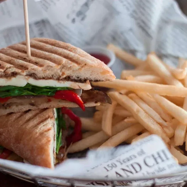 A halved panini with fries, served in a wire basket.