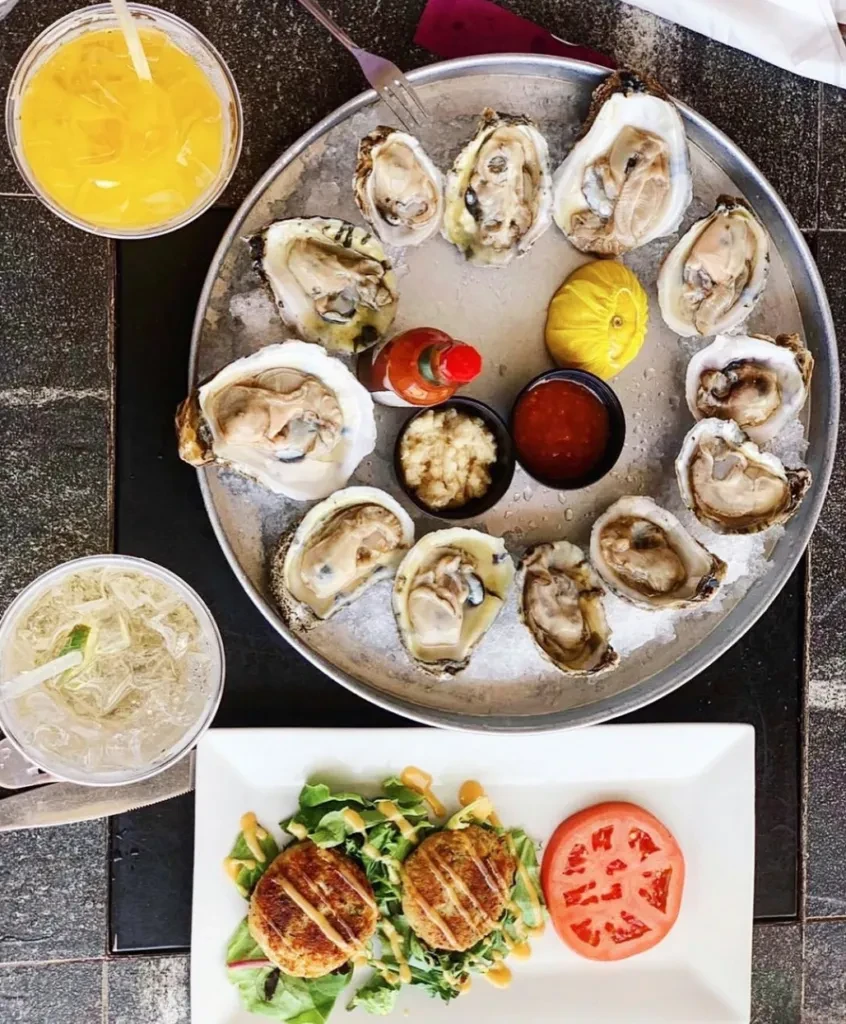 A platter of oysters with drinks and a side of crab cakes.