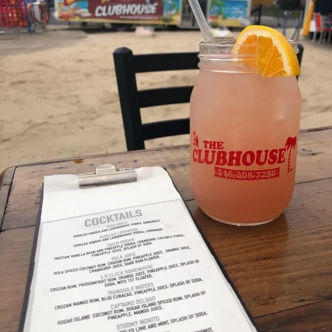 A pink cocktail and a menu with "COCKTAILS" on a wooden table.