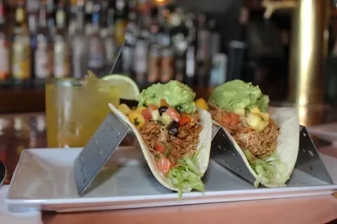 Two tacos with pulled pork, guacamole, and salsa, with a drink.