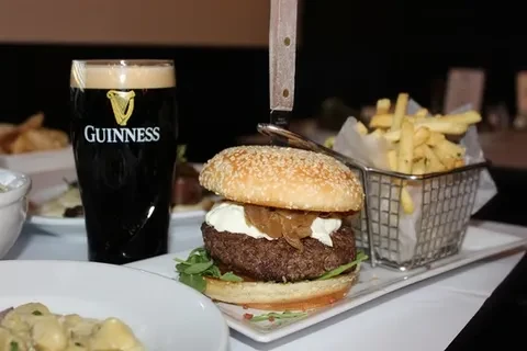 A burger with fries and a Guinness beer on a white table.
