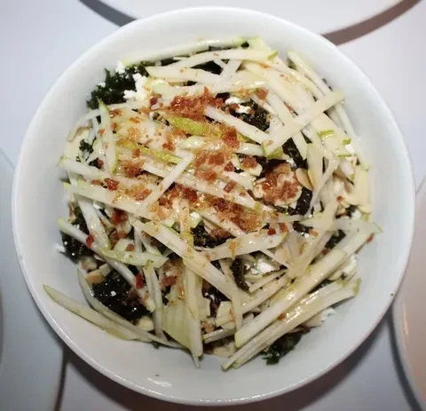 Overhead shot of a salad in a white bowl with green vegetables.