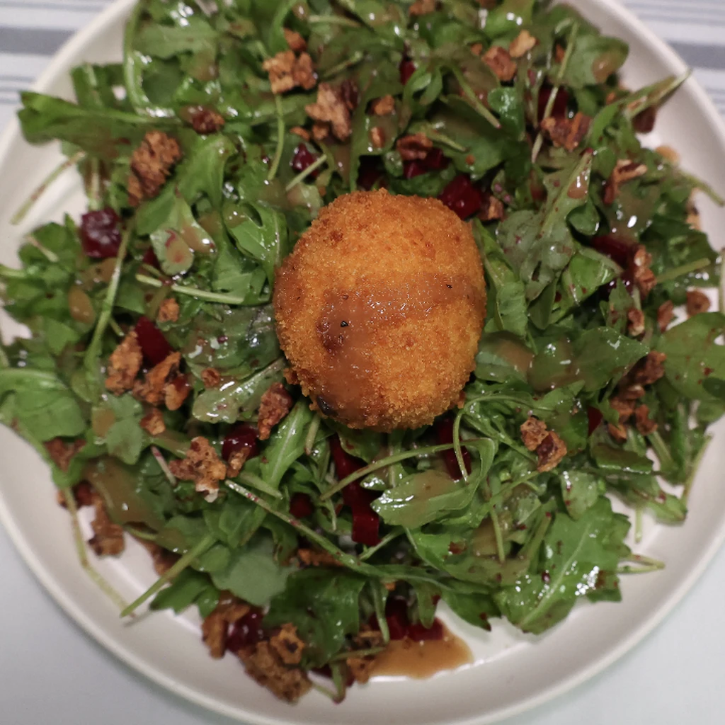 A breaded fried ball on a bed of arugula with nuts.