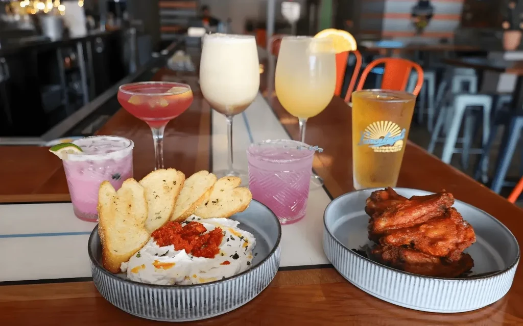 Drinks, chicken wings, and dips on a bar counter.