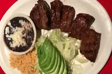 A plate with steak, black beans, rice, avocado, and shredded lettuce.