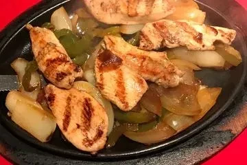 Chicken fajitas with grilled peppers and onions sizzling in a black pan.