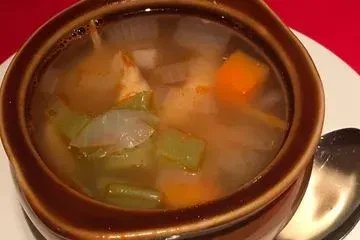 Brown bowl of vegetable soup with carrots, celery, and onions.