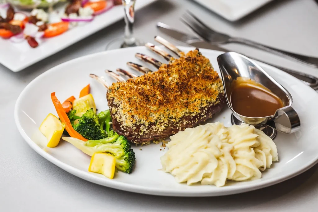 Plate of rack of lamb, mashed potatoes, vegetables, and gravy.