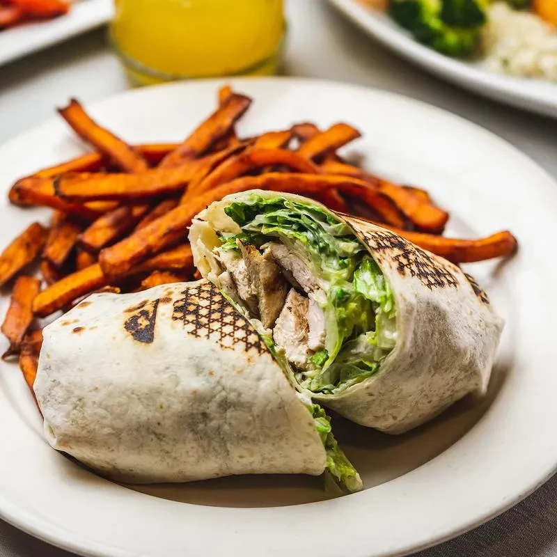 Chicken Caesar wrap cut in half with sweet potato fries.